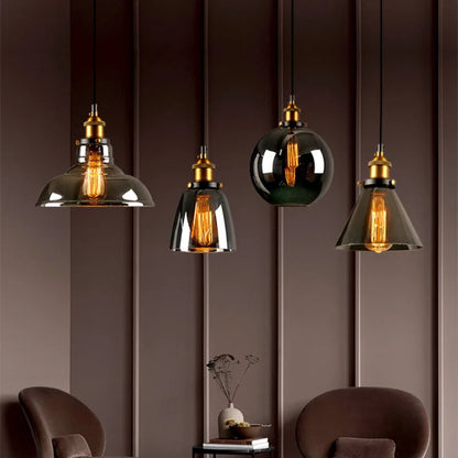Four smoke grey glass pendant lights in dome, bell, globe and cone shapes with brass fittings and Edison filament bulbs displayed against a moody dark brown paneled wall with velvet armchairs — LivDecor