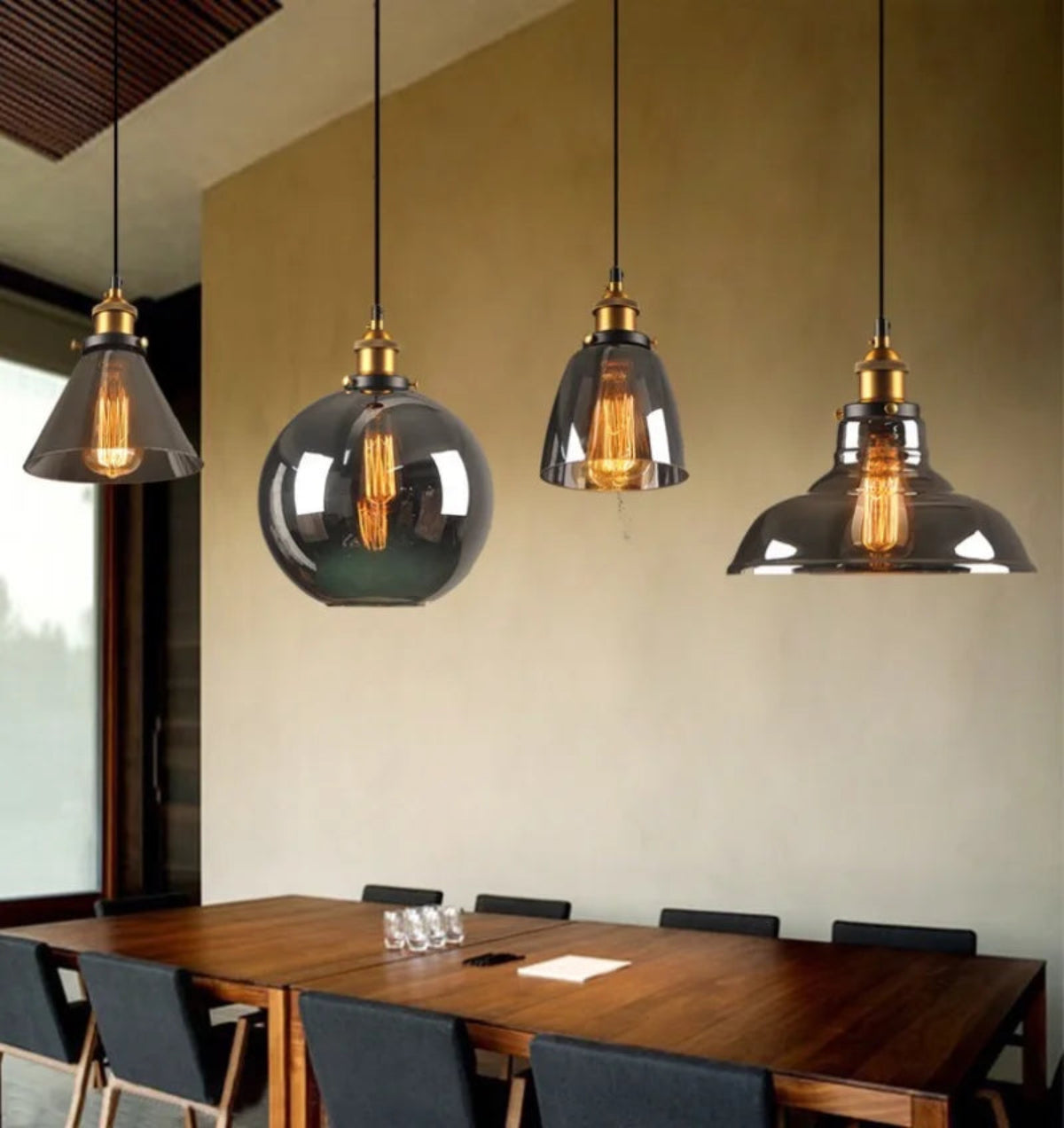 Four smoke grey glass pendant lights in cone, globe, bell and dome shapes with brass fittings and glowing Edison filaments above a walnut dining table with dark chairs and warm plaster walls — LivDecor