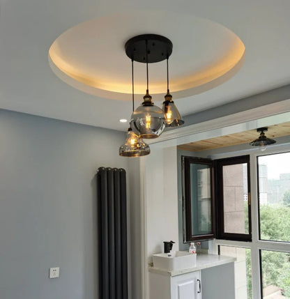 Three smoke grey glass pendant lights in bell, globe and dome shapes hung from a black round ceiling plate within a warm-lit tray ceiling in a real home installation — LivDecor