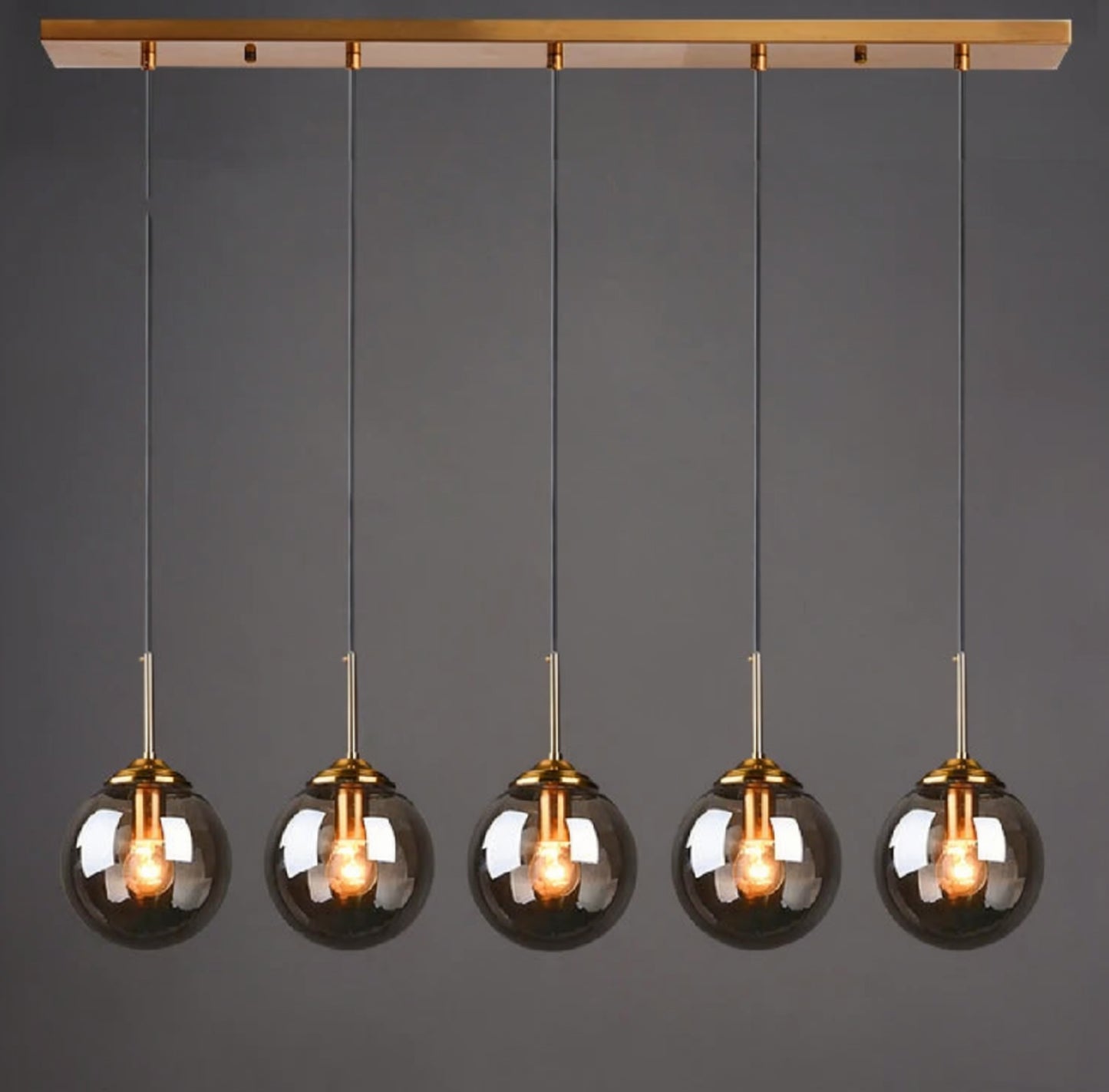 Smoky grey glass globe pendant light, 5-light linear configuration on a gold bar mount, lit against a dark grey background — LivDecor