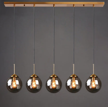 Smoky grey glass globe pendant light, 5-light linear configuration on a gold bar mount, lit against a dark grey background — LivDecor
