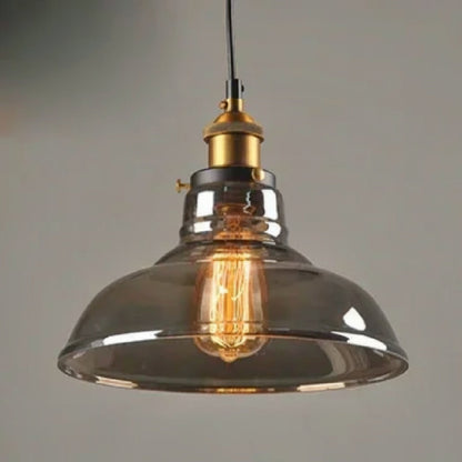 Smoky grey glass industrial dome pendant light with brass Edison fitting and lit filament bulb glowing warmly against a grey background — LivDecor
