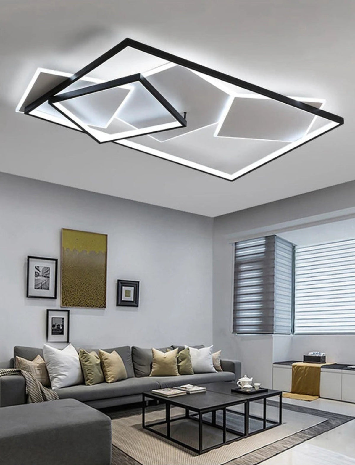 Strata Linear geometric LED chandelier in matte black glowing cool white in a modern living room with grey sectional sofa, gold abstract art, gallery wall, and roller blinds — LivDecor
