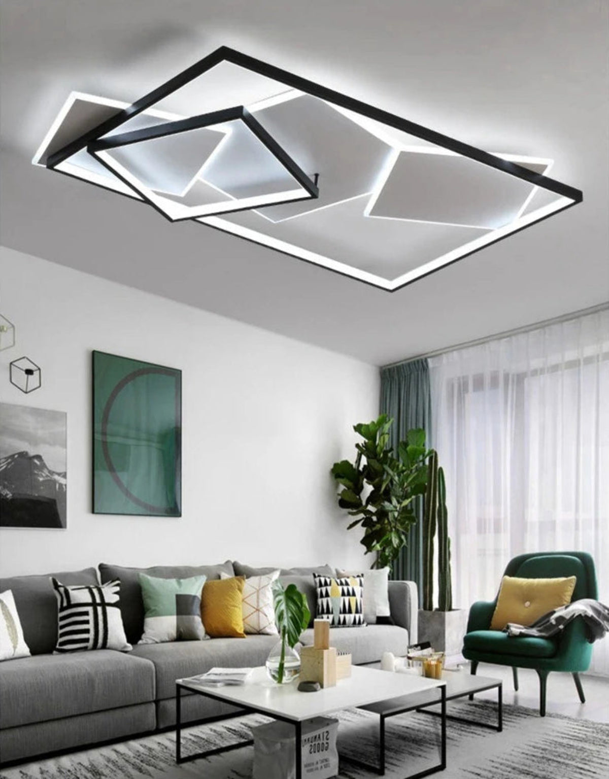 Strata Linear geometric LED chandelier in matte black glowing cool white in a modern Scandinavian living room with grey sofa, emerald green armchair, tropical plants, and teal curtains — LivDecor
