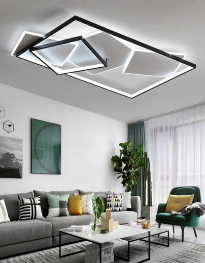 Strata Linear geometric LED chandelier in matte black glowing cool white in a modern Scandinavian living room with grey sofa, emerald green armchair, tropical plants, and teal curtains — LivDecor

