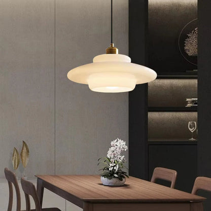 White glass tiered saucer pendant light with brass fitting above a wood dining table with grey paneled walls, dark cabinetry, an orchid centerpiece, and gold leaf decor — LivDecor