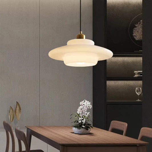 White glass tiered saucer pendant light with brass fitting above a wood dining table with grey paneled walls, dark cabinetry, an orchid centerpiece, and gold leaf decor — LivDecor